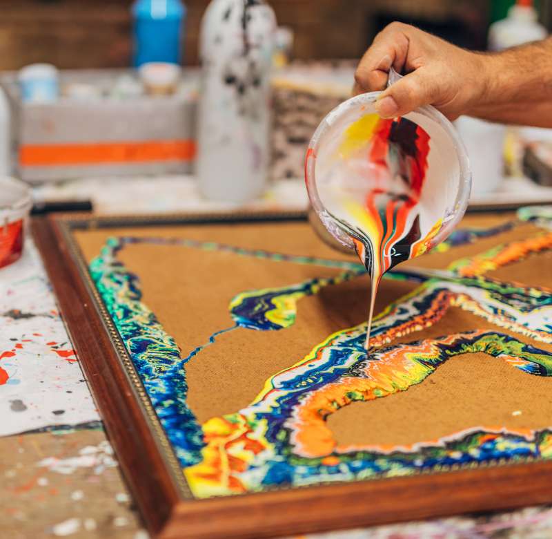 an image of someone pouring acrylic paint into a special wood frame. The paint and finished painting will look marbled. 